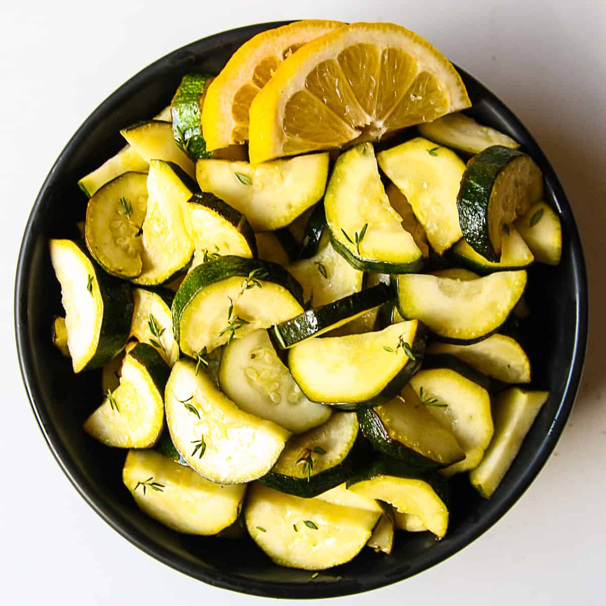 Air fryer zucchini slices in a black bowl with lemon wedges.