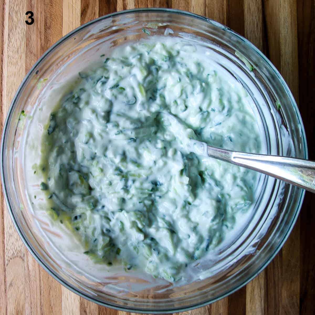 The finished tzatziki sauce with all the ingredients stirred together in a glass bowl.