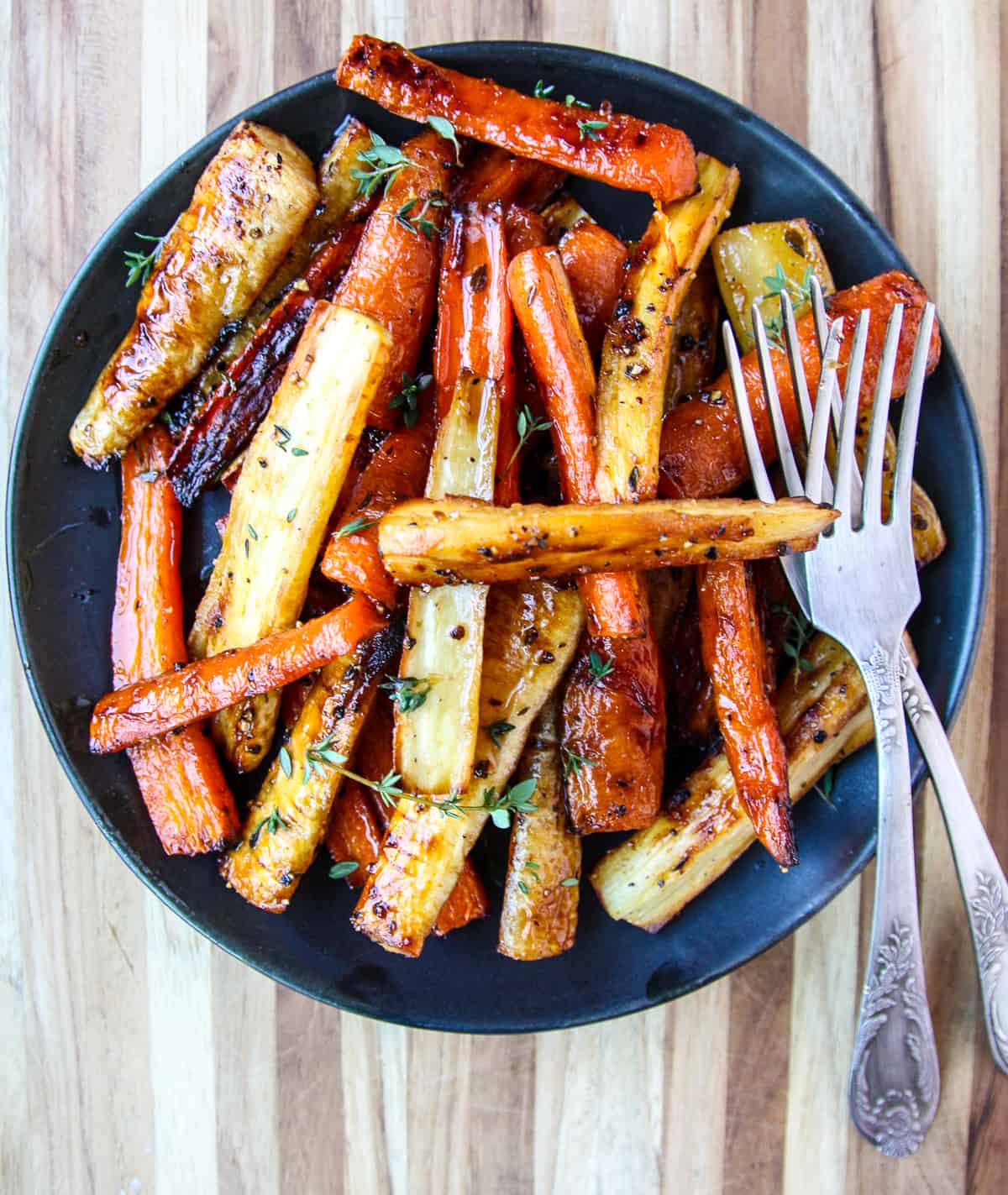 Honey roasted carrots and parsnips on a black plate with two silver forks.