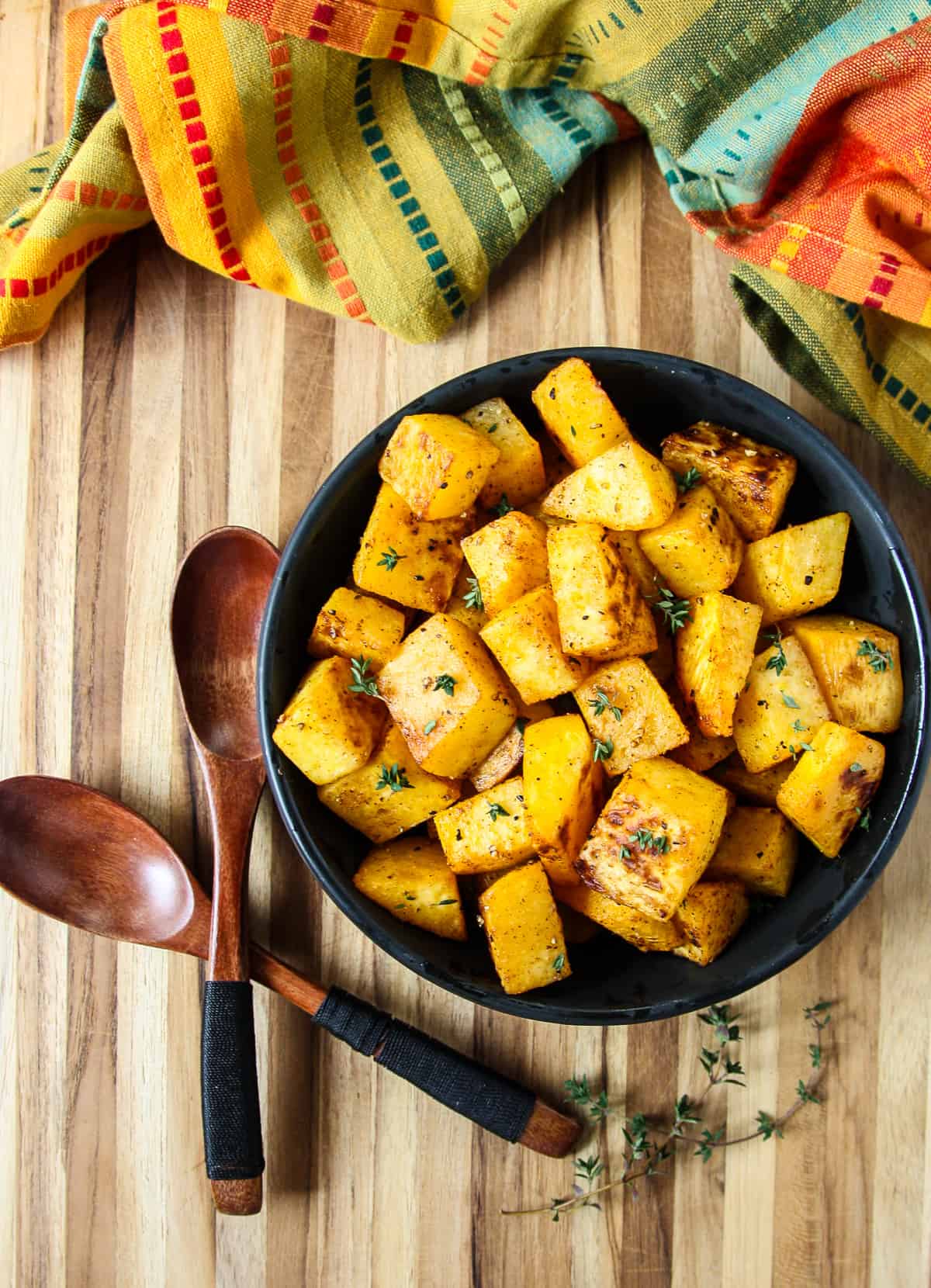 Roasted rutabaga cubes in a black bowl and two wooden spoons on a wooden board.