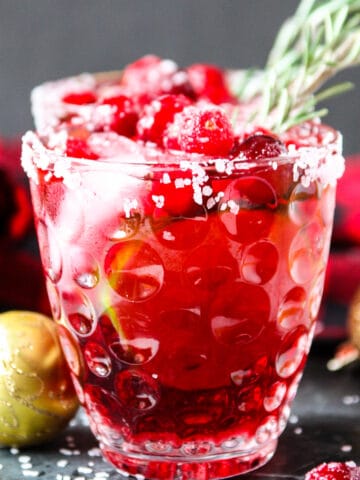 A cranberry mistletoe margarita in a glass with a sprig of rosemary.