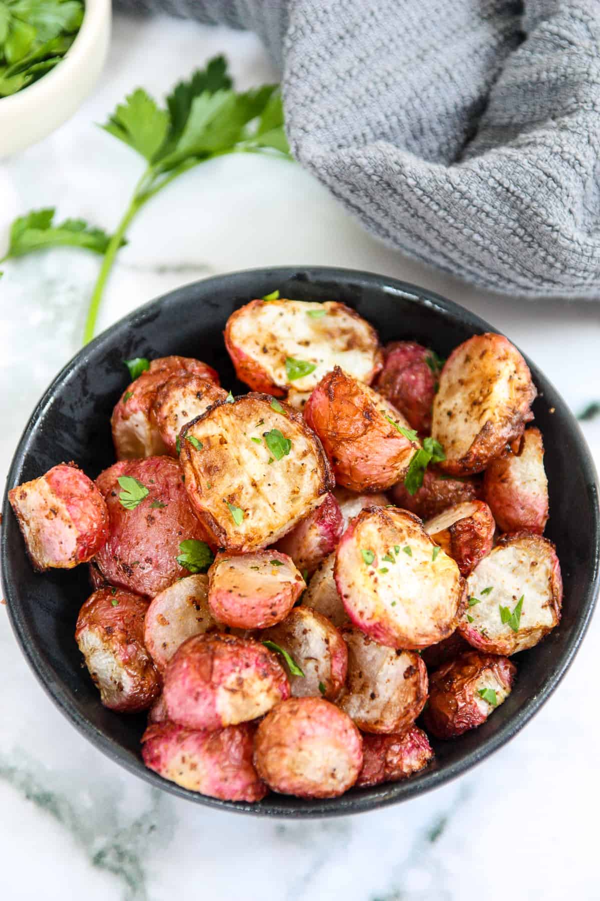 A bowl of air fryer radishes on a marble countertop.