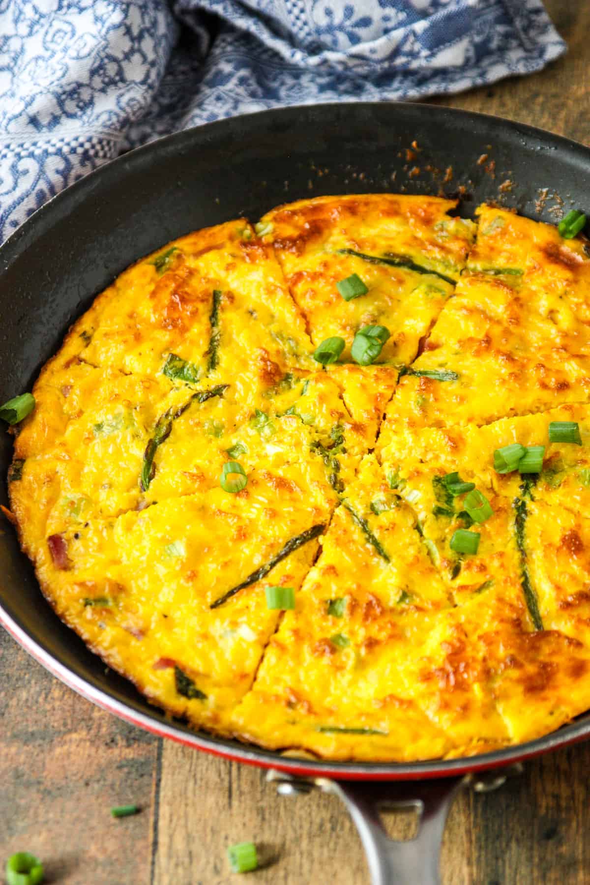 Baked ham and cheese frittata in a skillet, garnished with green onion slices.