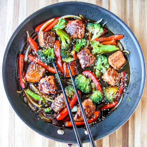Salmon stir fry being cooked in a black skillet.