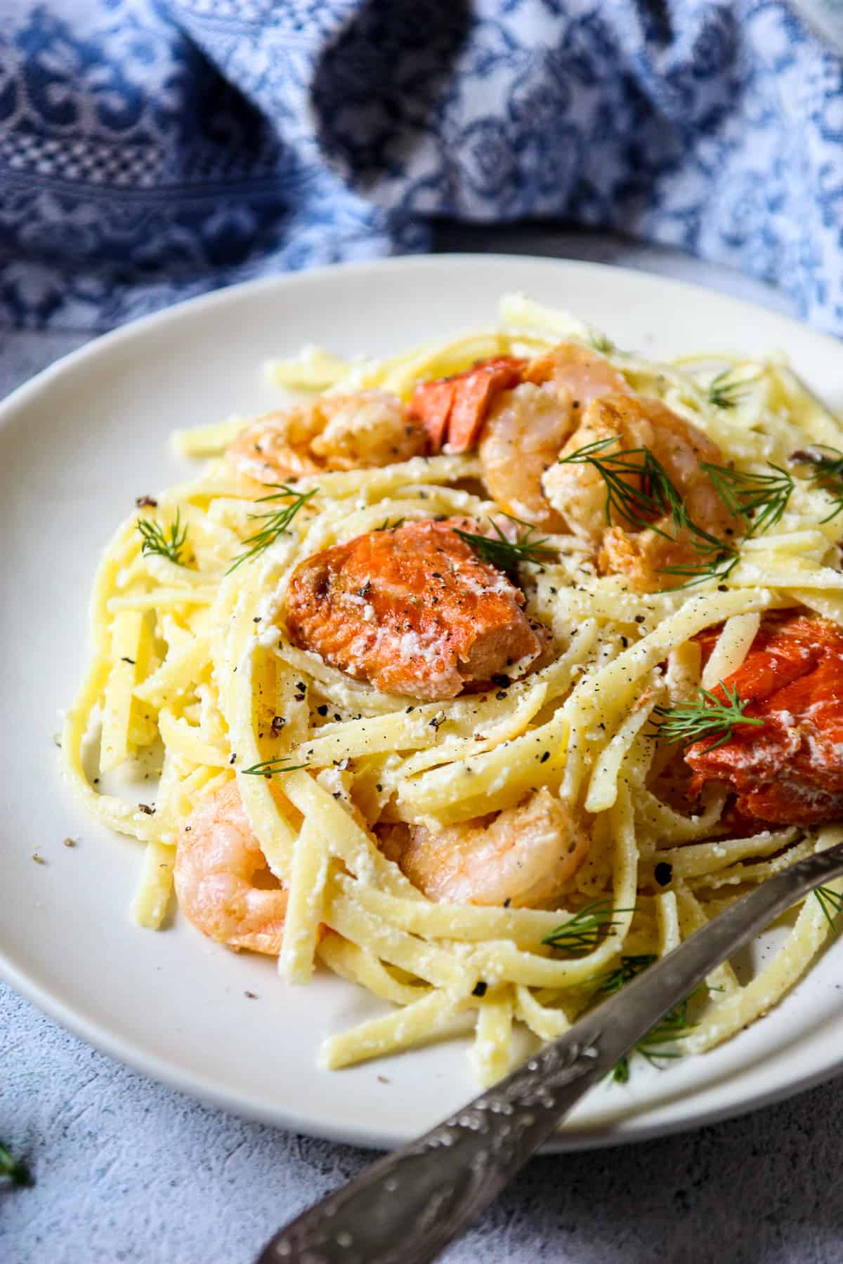 Shrimp, salmon chunks and fettuccini noodles on a white plate with a silver fork.