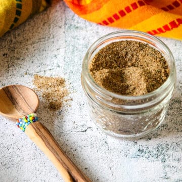 An open jar of Jamaican jerk seasoning next to a small wooden spoon.