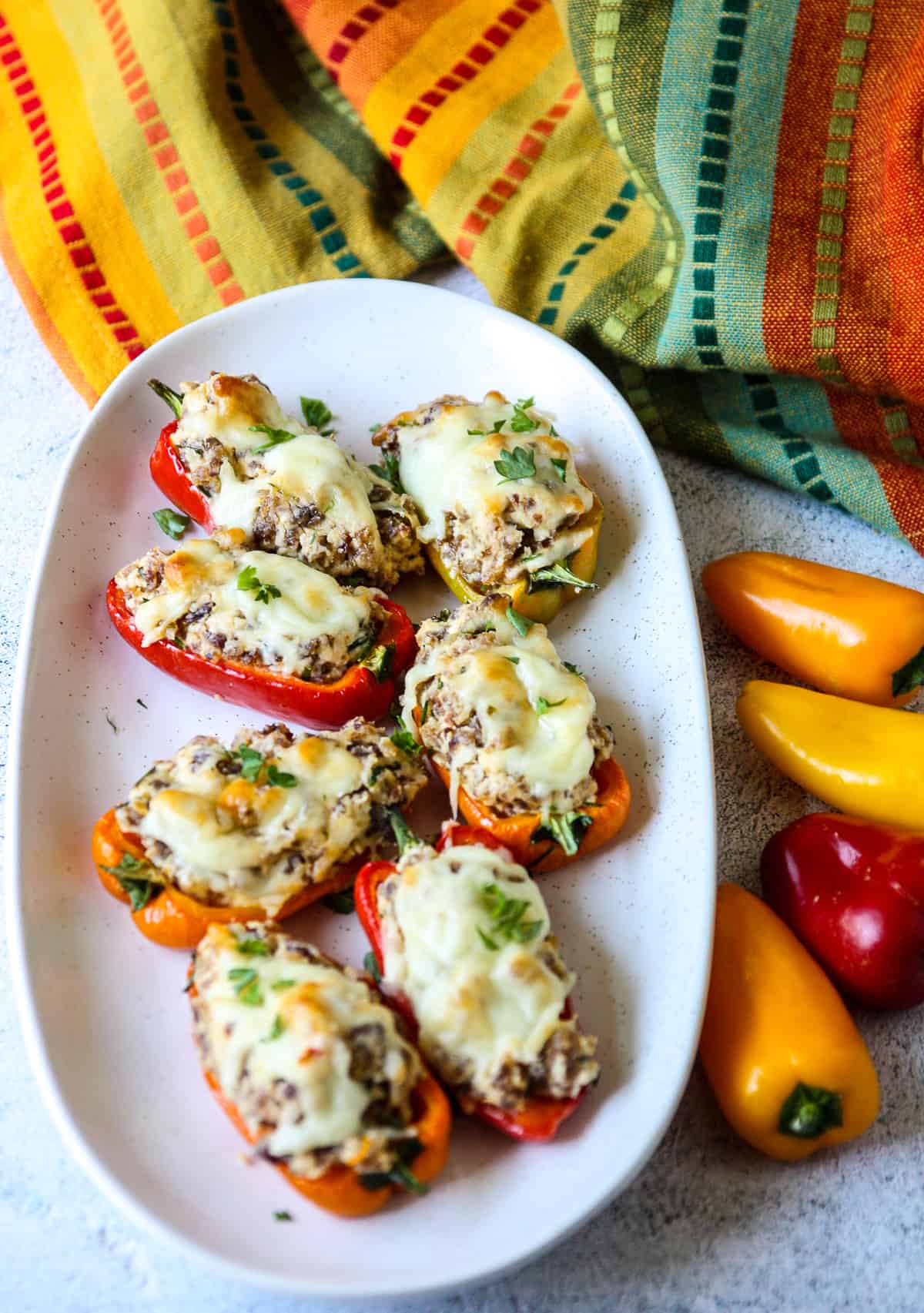 Sausage stuffed mini peppers on a serving platter, beside some fresh whole mini peppers.