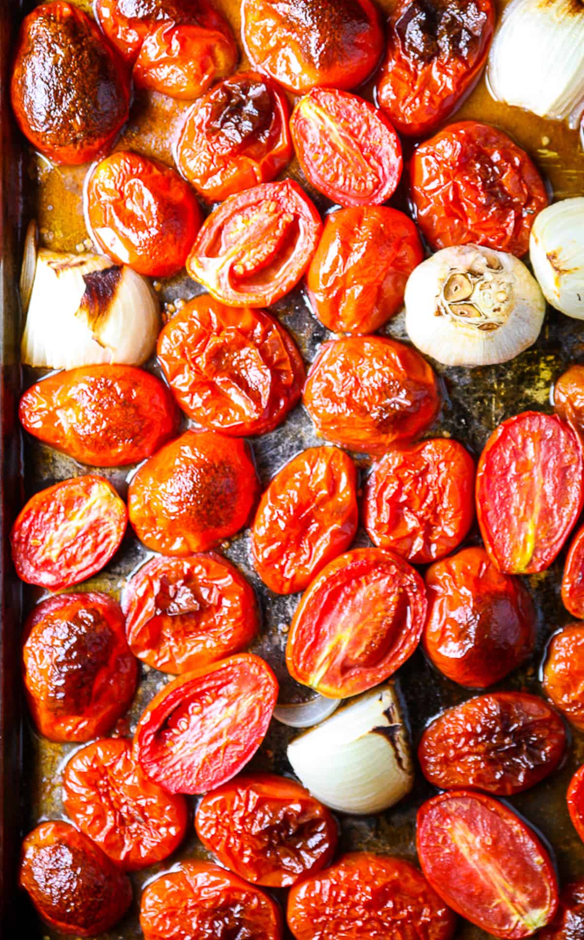 Tomatoes, onion, and garlic on a baking sheet after roasting.
