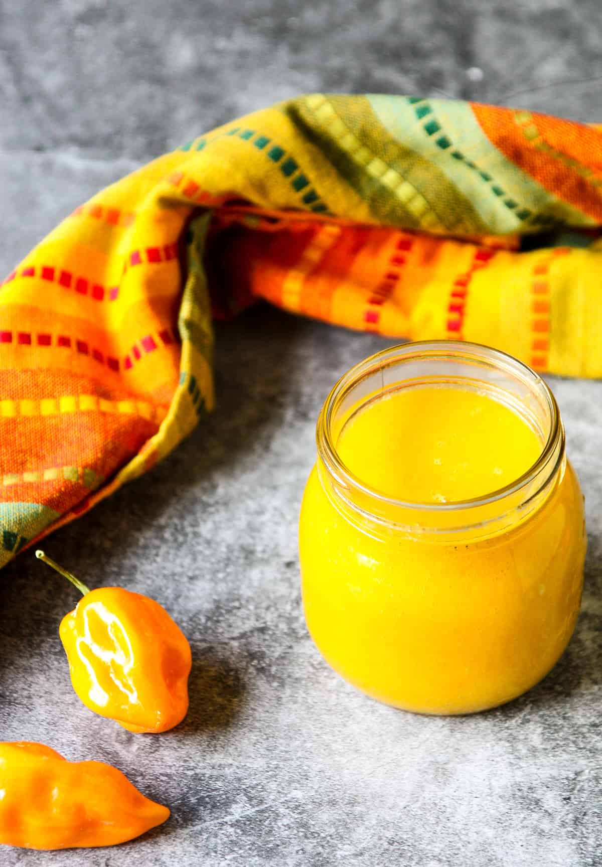 Habanero peppers next to a glass jar of mango habanero hot sauce and a multi colored napkin.