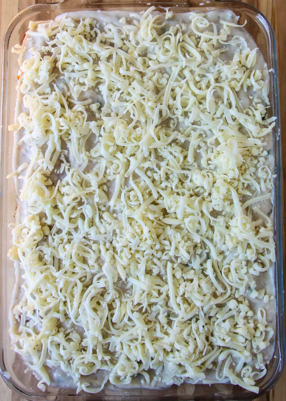 A final layer of shredded mozzarella cheese tops the assembled white vegetable lasagna.