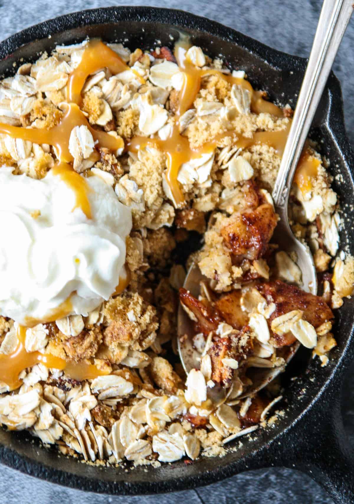A spoon scooping out a bite from a pan of apple crisp.