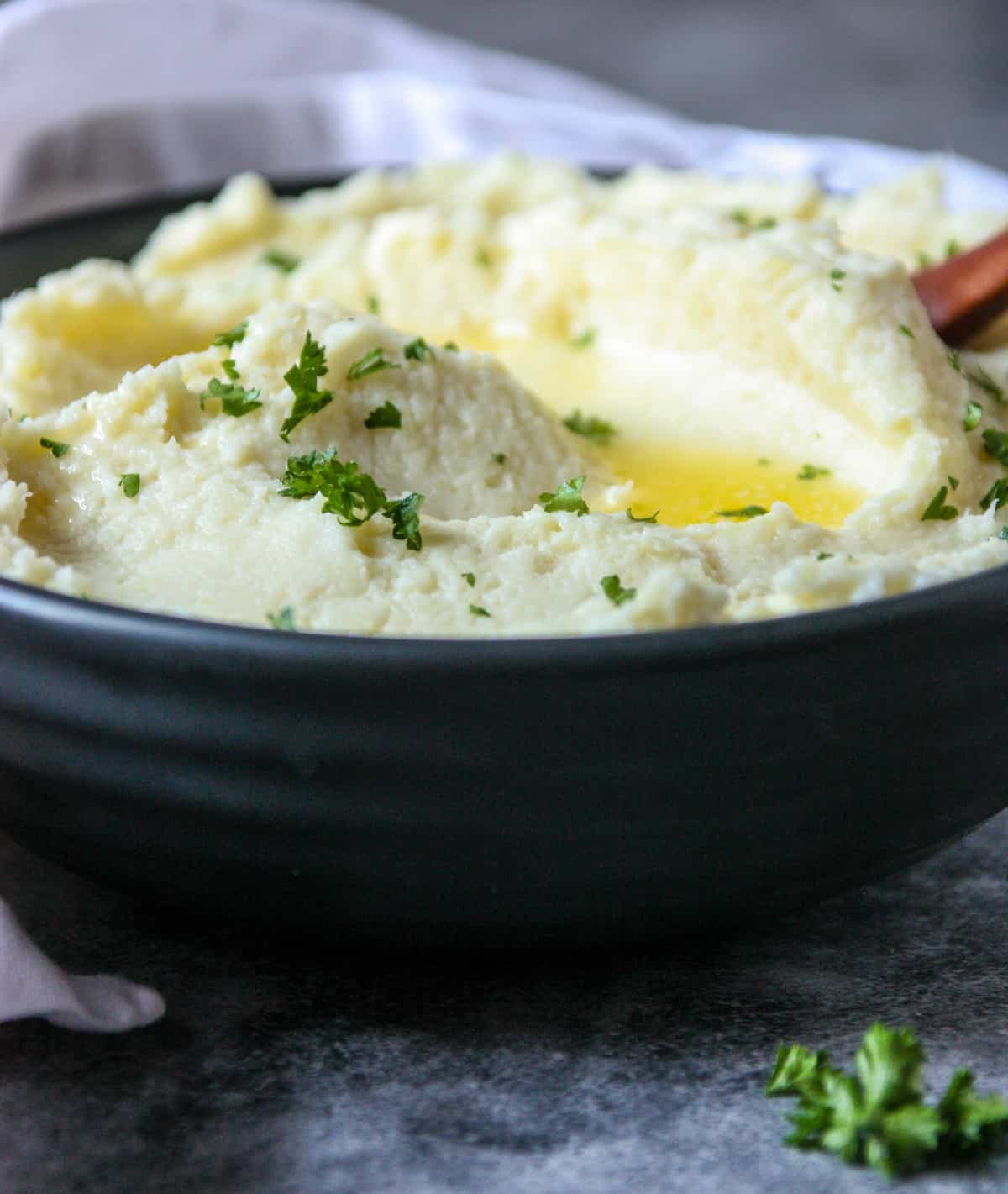 Parsnip puree with butter and parsley in a black dish.