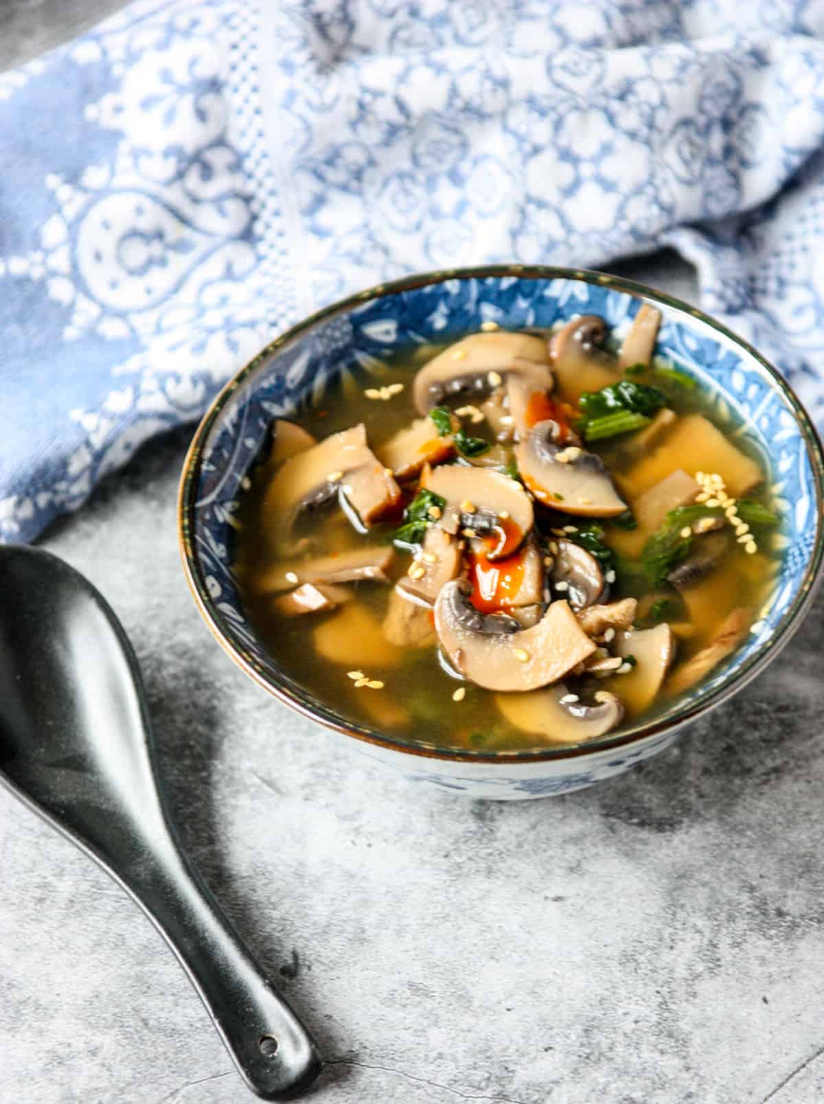 Mushroom miso soup in a blue and white bowl next to a blue and white napkin.