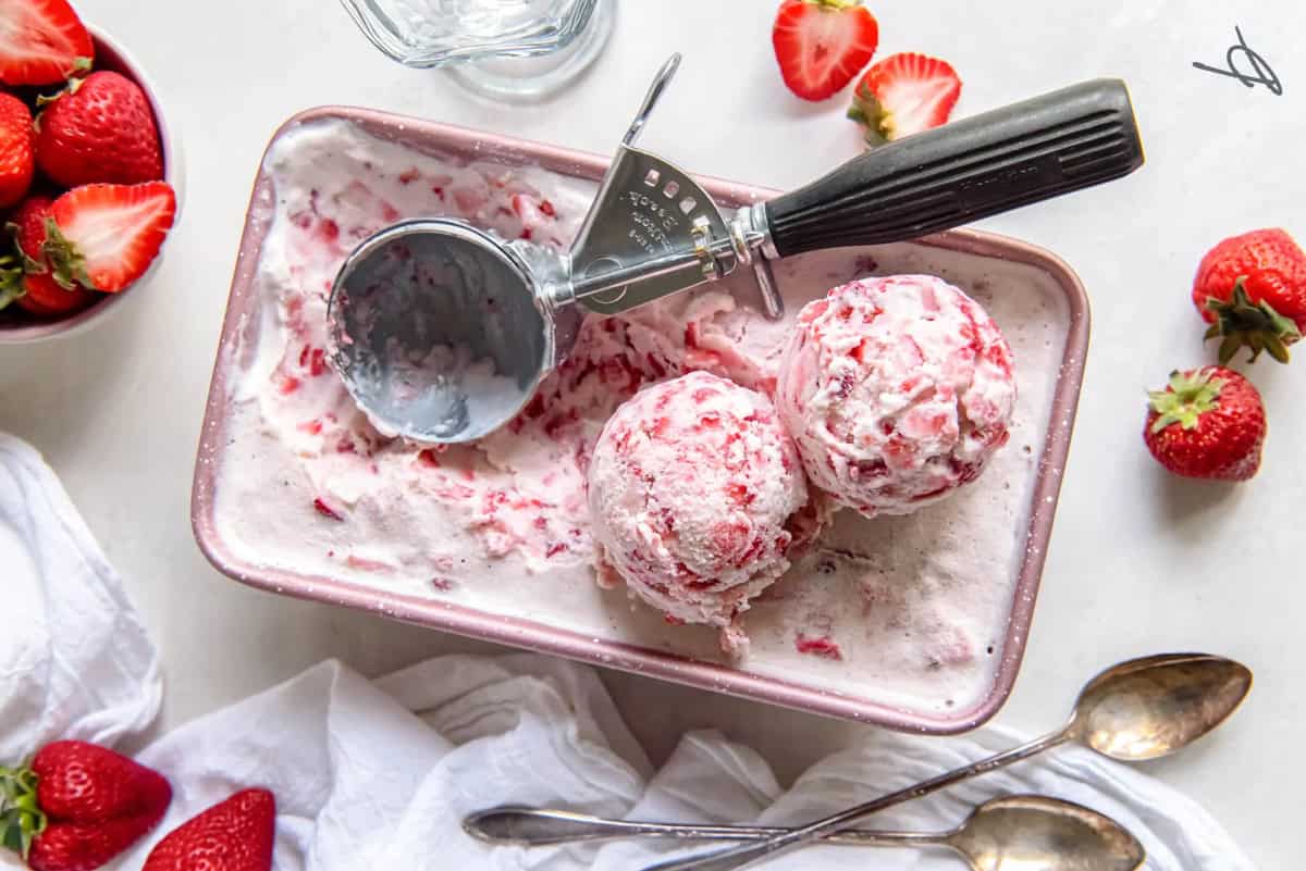 Strawberry ice cream in a loaf pan with an ice cream scoop.