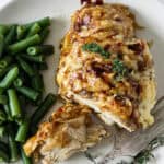French onion chicken on a white plate with green beans.
