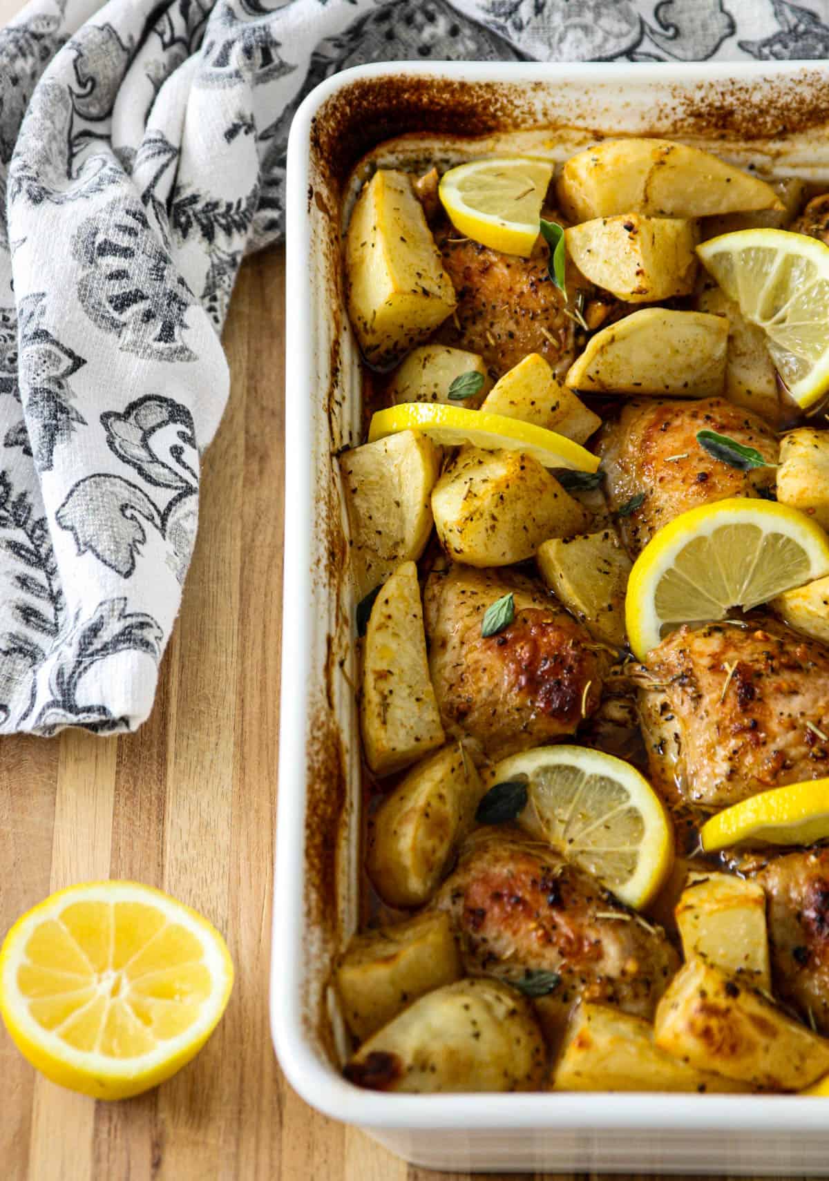 A pan of baked Greek lemon chicken and potatoes on a wooden cutting board.