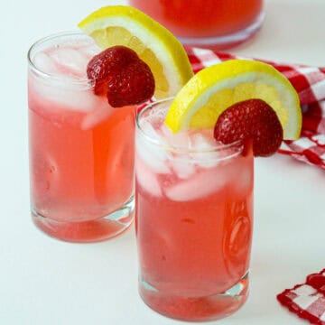 Two glasses of rhubarb lemonade, garnished with lemon slices and strawberries.
