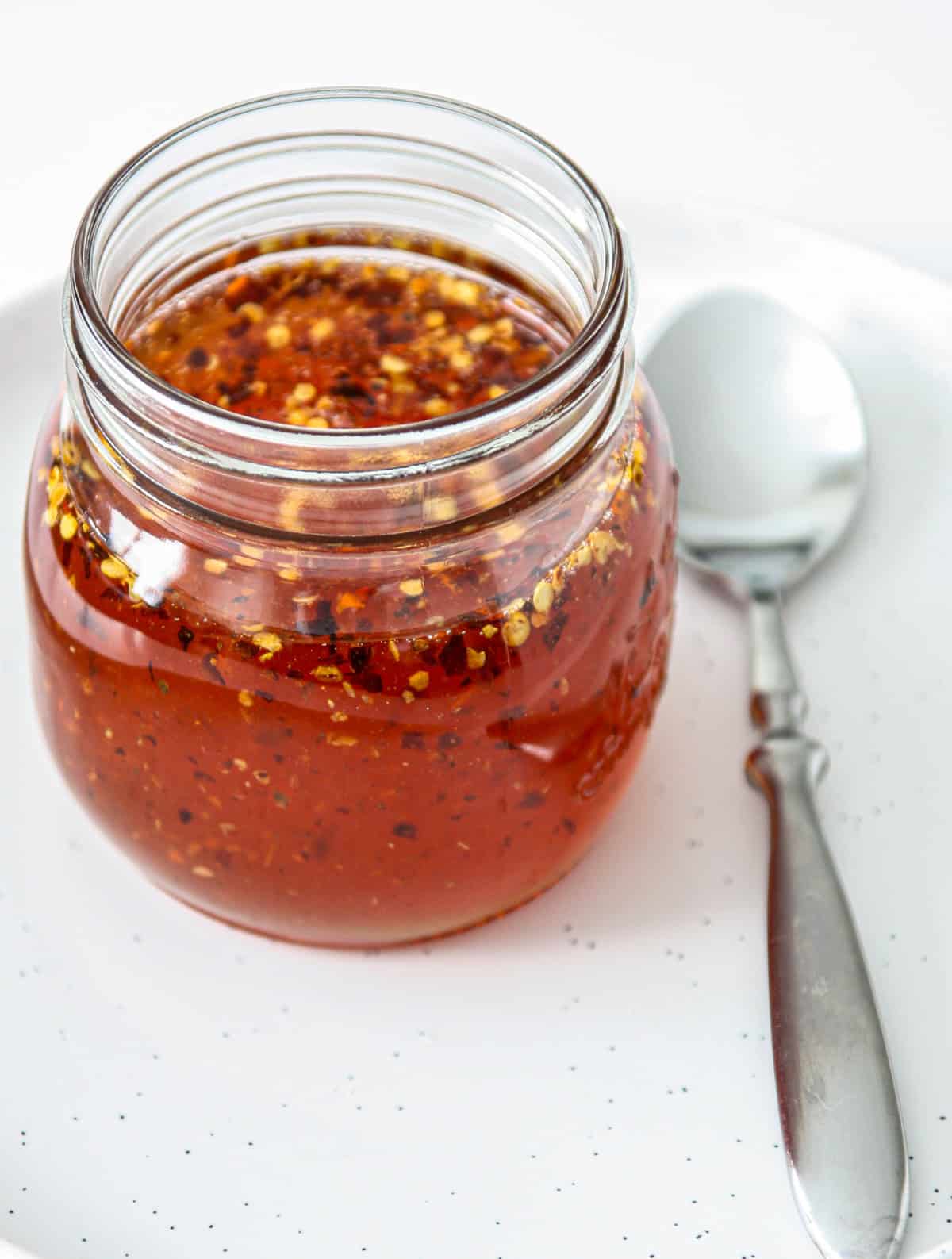 Hot honey in a glass jar next to a silver spoon.